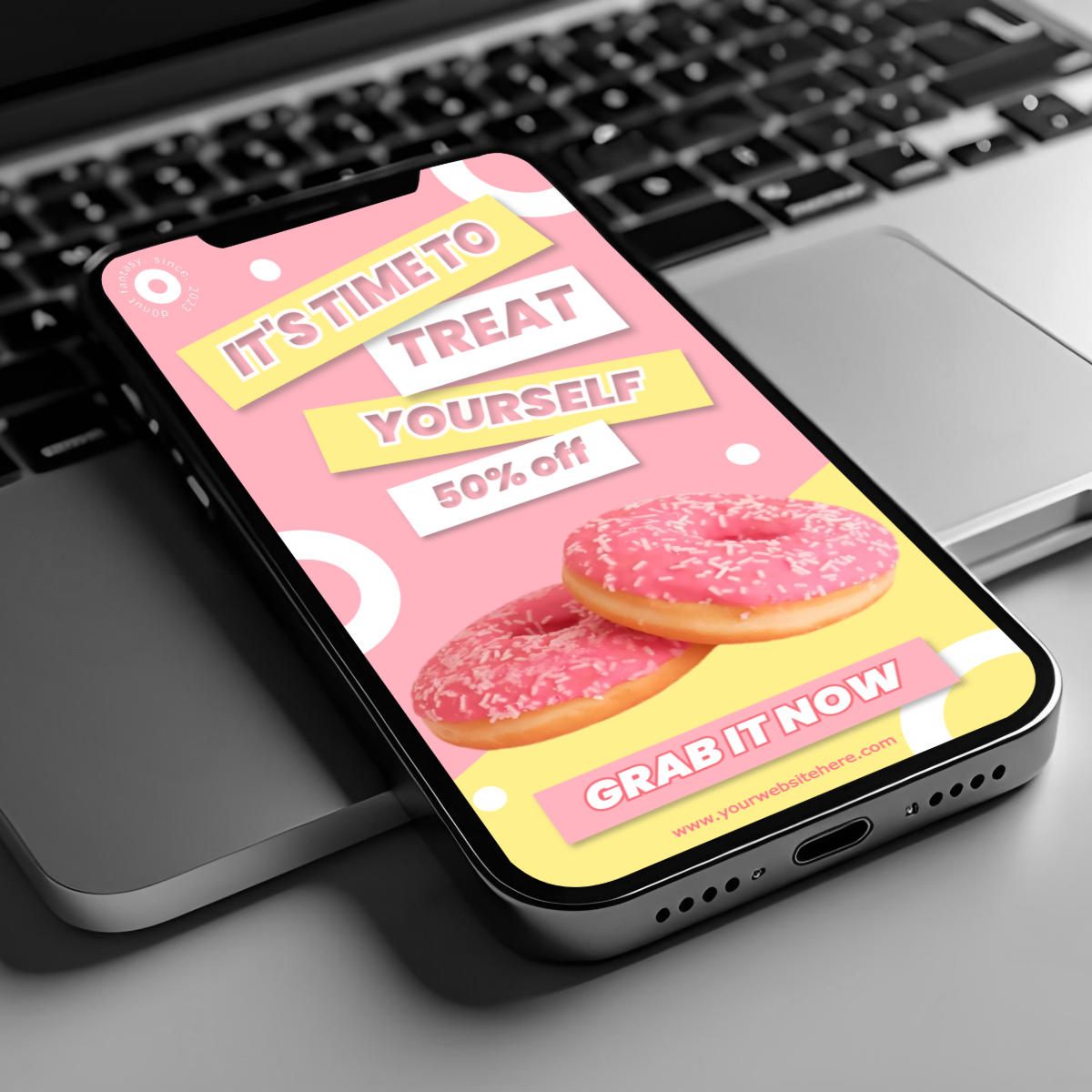 A phone on a laptop displays a bold pink donut promo with bright text saying “It’s time to treat yourself” and “Grab it now” at 50 percent off.